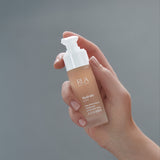Hand holding a RUA Hydrate Elixir against a gray background