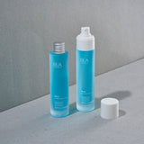 Two RUA Mist bottles, one with an aluminium cap, and the other with a spray top cap, on a gray surface with a gray background