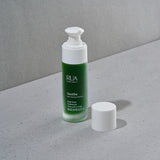 RUA Soothe Softening Serum bottle with white reusable pump on a gray surface