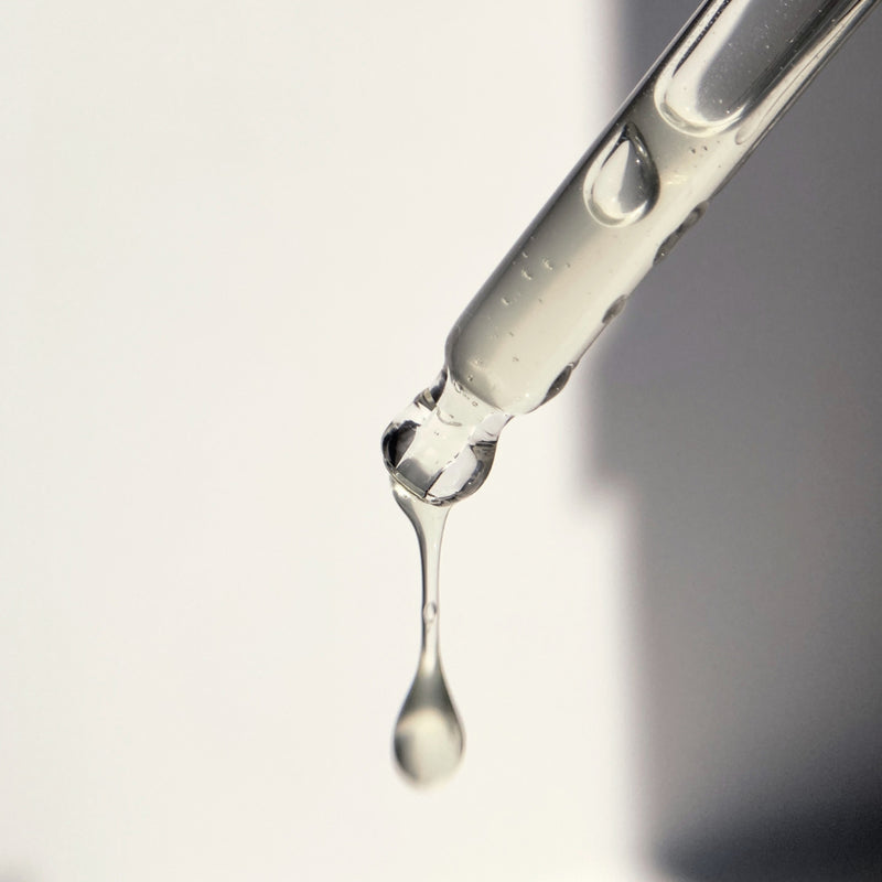 Close-up of glass dropper with Hydrate Elixir dripping against a gradient background