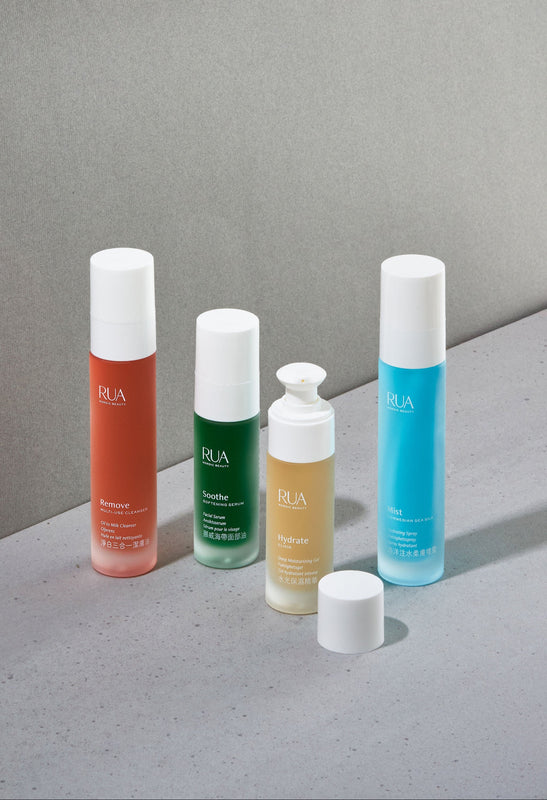 All four RUA skincare bottles with white caps on a gray surface and background