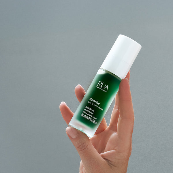 Hand holding a RUA Nordic Beauty  Soothe Serum bottle with white reusable pump against a gray background